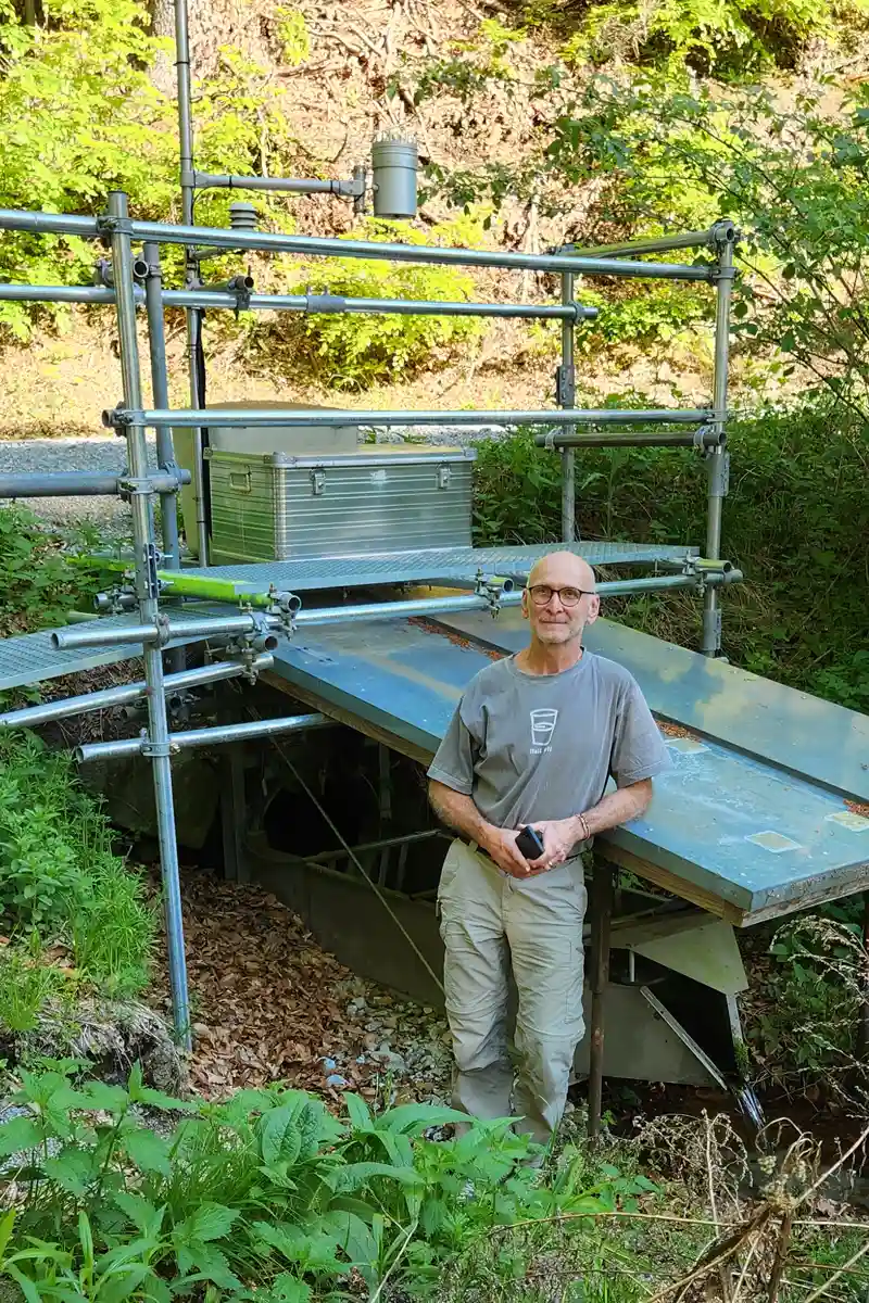 A researcher beside ecosystem monitoring instrumentation in a forest setting.